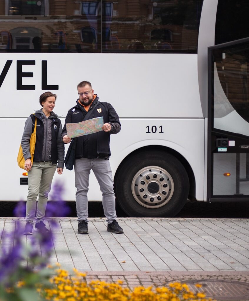 Kaksi matkaopasta katsoo karttaa, taustalla bussi.